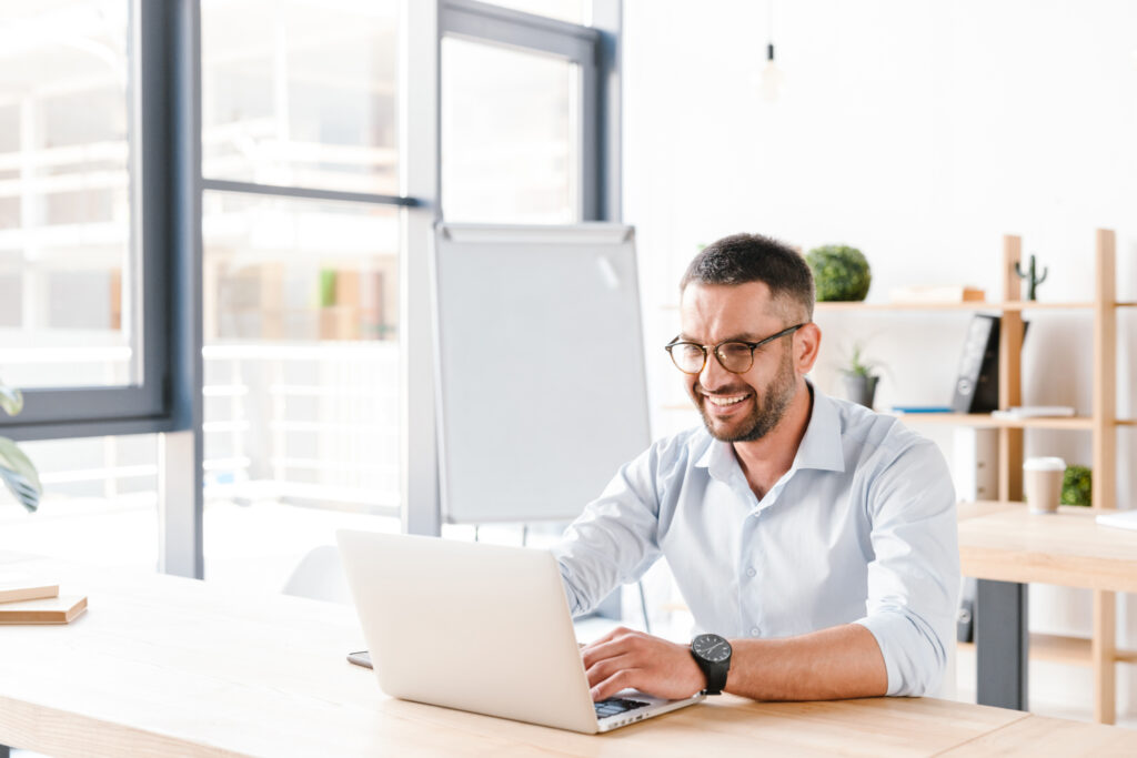 Photo of joyous office man 30s in white shirt sitting at desk