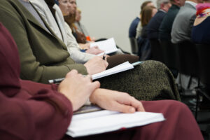KI Konferenz - Teilnehmende mit Notizbüchern während einer Keynote
